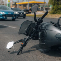 A fallen motorcycle lies on its side on a busy road, with cars and a gas station in the background, conveying a scene of a recent accident. A fallen motorcycle lies on its side on a busy road, with cars and a gas station in the background, conveying a scene of a recent accident.